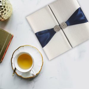 white silk invitation with navy blue ribbon and pair brooch