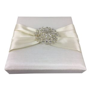 White boxed wedding invitation with ivory ribbon and brooch